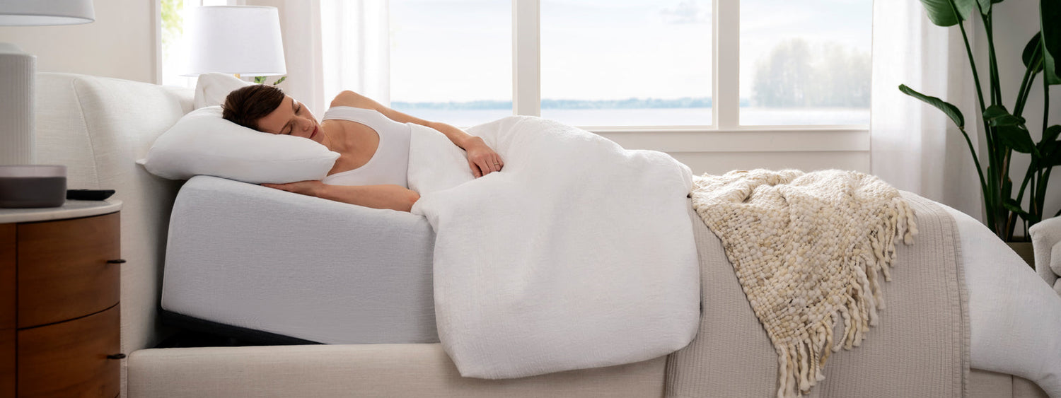 Woman lying in bed with adjustable base and white bedding in a bright bedroom