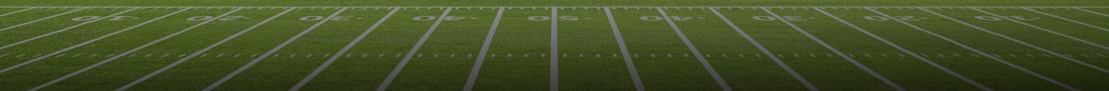 A low-angle, wide view of an American football field with white yard lines and markings on green turf.