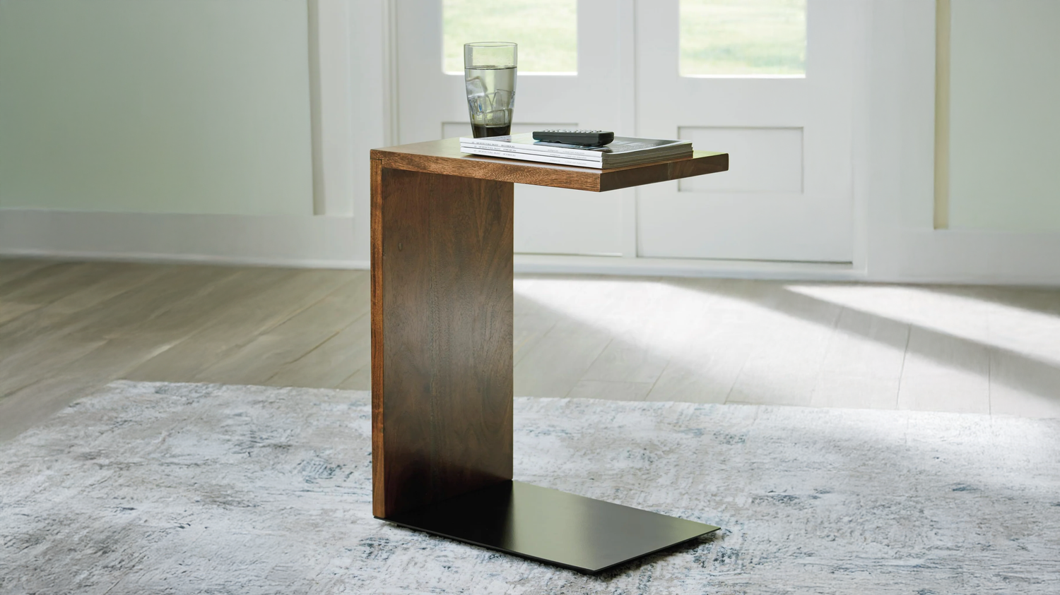 Wooden side table with a glass and remote control on a light-colored rug.
