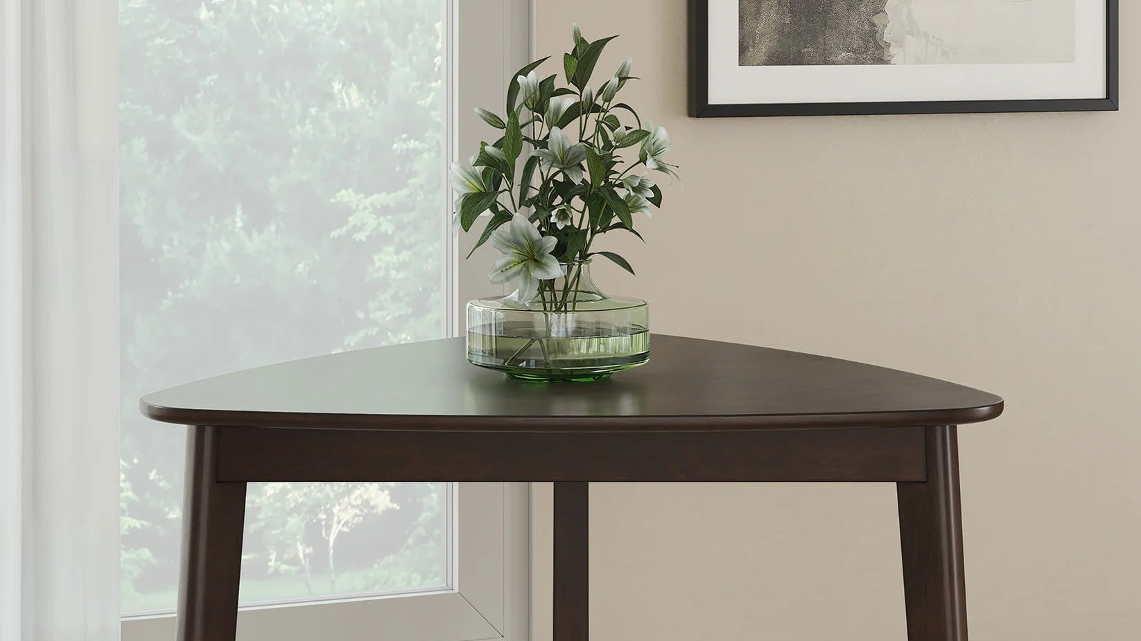 Wooden dining table with a vase of flowers in a room with a window and framed picture on the wall.