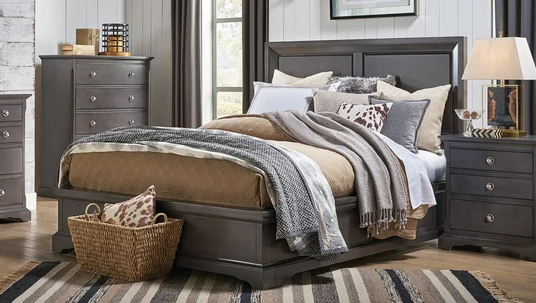 A dark gray wood bed frame with a high panel headboard and matching footboard, styled with beige and gray bedding, pillows, and a textured throw blanket in a bedroom setting.