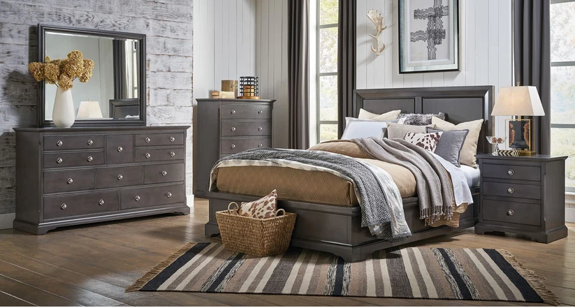 A dark gray wood bedroom furniture set including a bed frame, matching nightstands, a dresser, and a tall chest, styled in a rustic modern bedroom with wood floors, a striped rug, and neutral bedding.