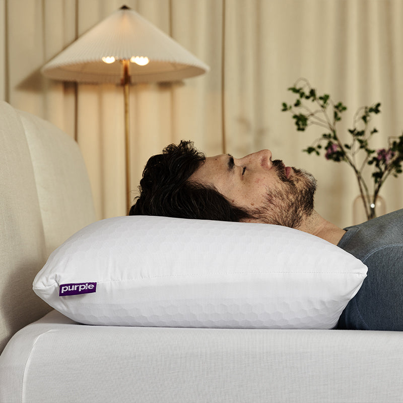 Person lying on a bed with a purple pillow, with a blurred background
