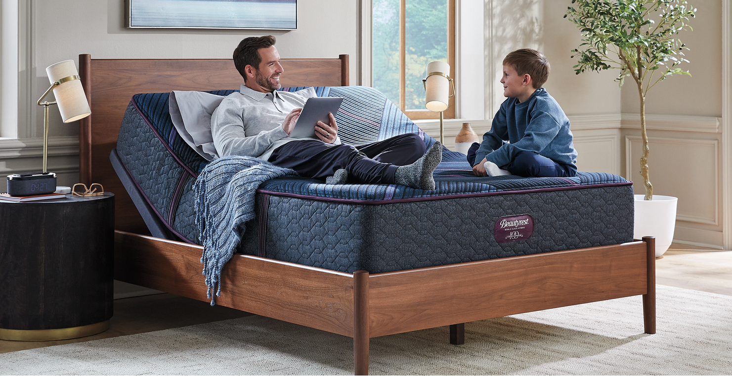 Man and child sitting on a bed in a bedroom with a mattress brand logo visible