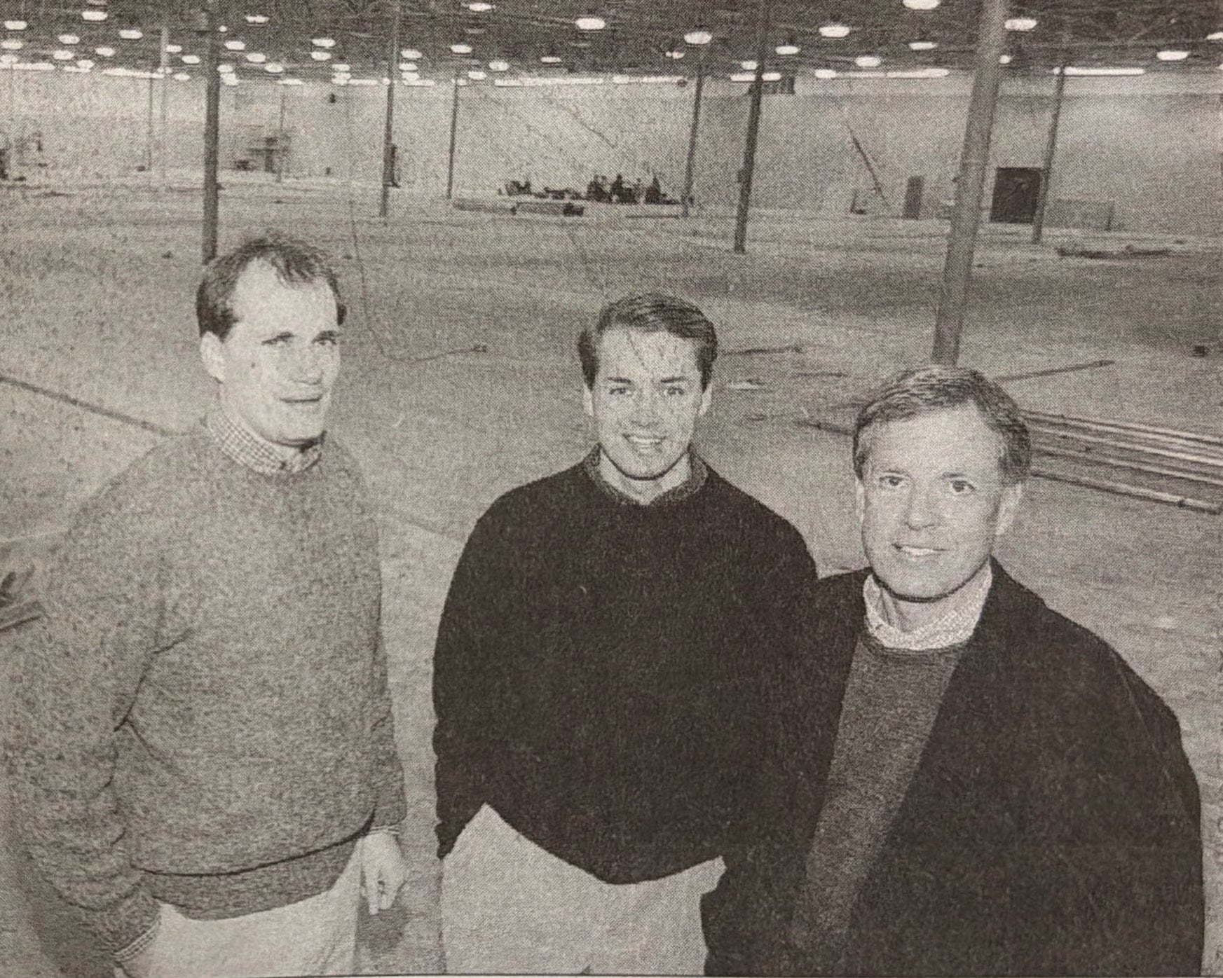 A scanned vintage newspaper page with a black-and-white photo of three men in a large empty store